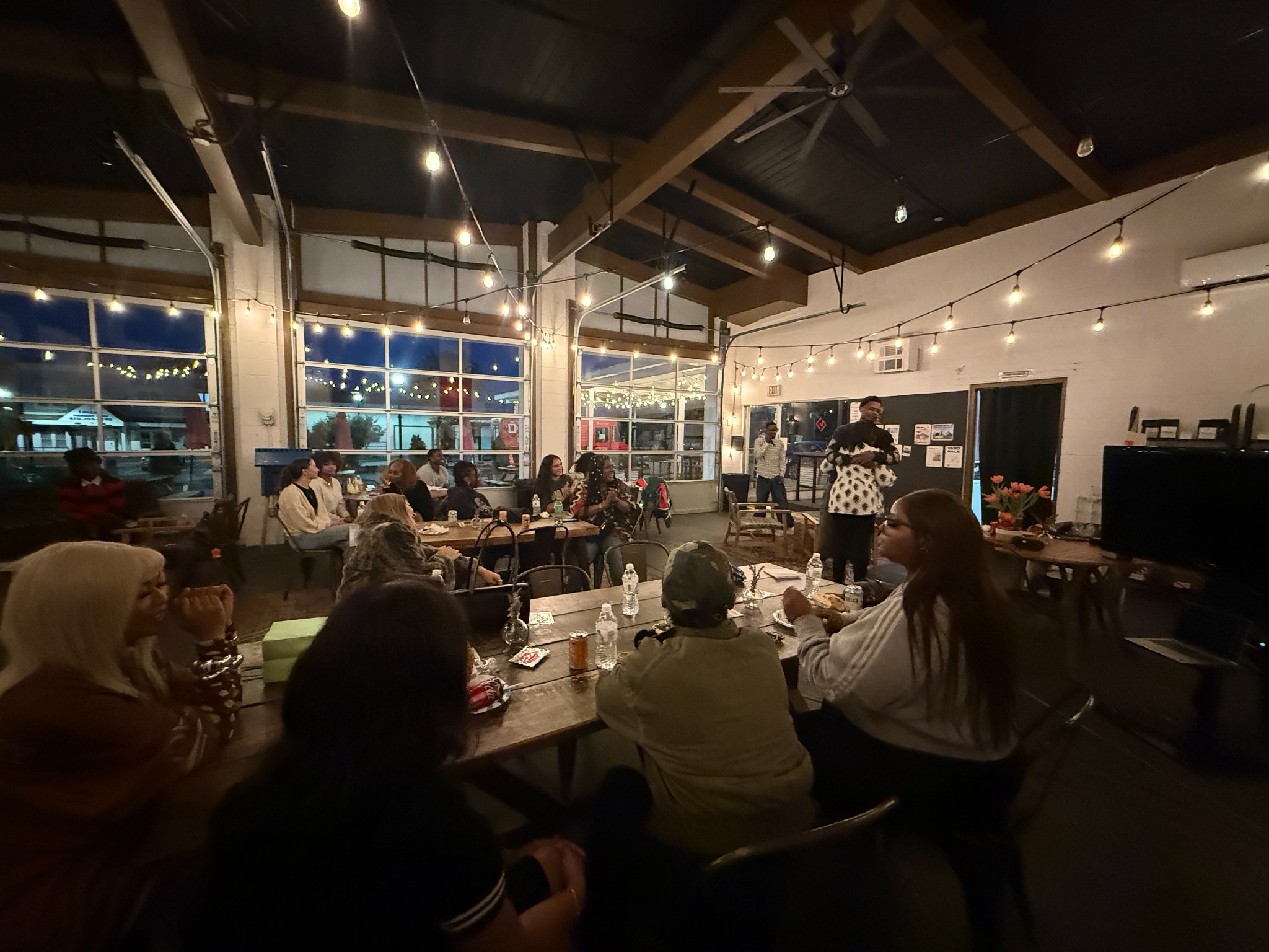 Community members gathered around tables for fellowship beneath string lights
